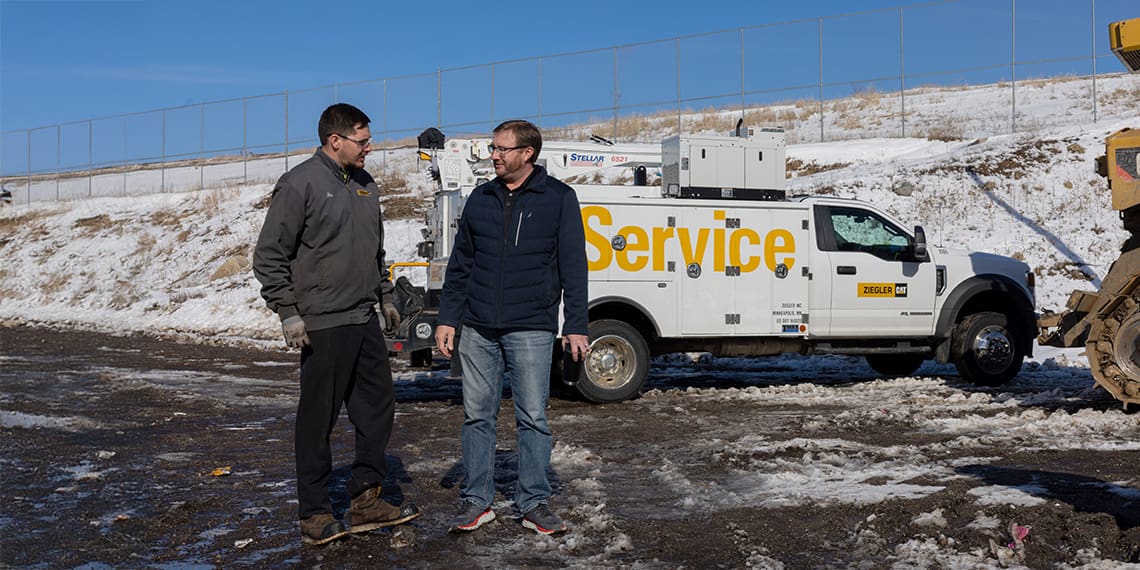 Two men conversing near a landfill in wintery conditions. A Stellar TMAX1 with a 6521 crane is in the background.